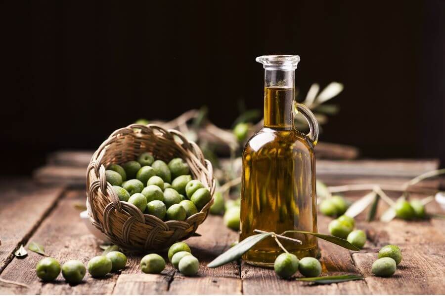 Erken hasat edilmiş bir sepet dolusu yeşil zeytin ve sıkıldıktan sonra şişelenmiş sızma zeytinyağı cam şişede yan yana