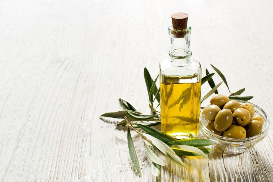 cam şişede natürel sızma zeytinyağı ve yanında cam kasede taze yeşil zeytin 