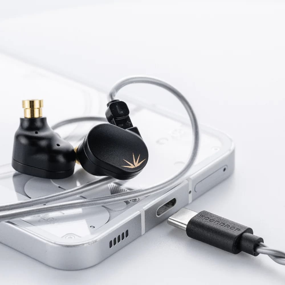 Moondrop Chu II DSP'nin USB-C ucu telefonun USB-C girişinin önünde, telefonun üstünde siyah kulaklıklar