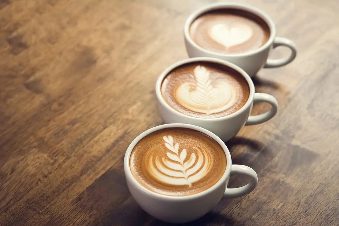 Ahşap masa üzerinde üç fincan latte artlı kahve – evde kahve demleme yöntemleri