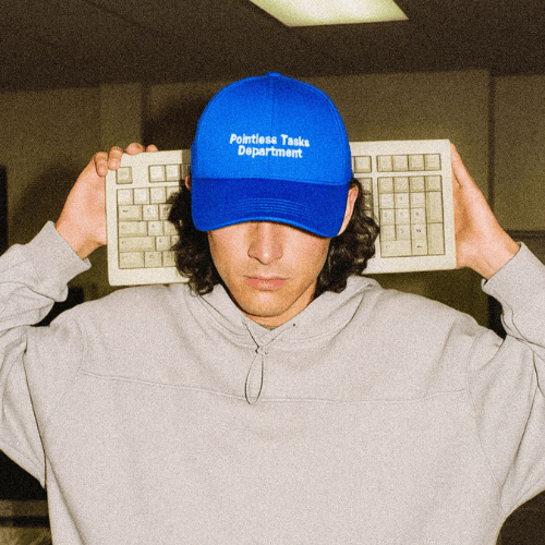 Ofice worker wears blue baseball cap and he is holding a keyboard
