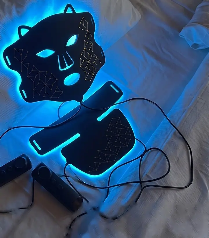Radiance maske ve boyun modülü yatağın üstünde, mavi ışıkta, iki kumandasıyla